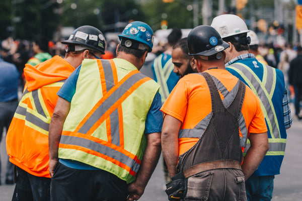 Back view of a diverse, experienced construction and fit-out team wearing hard hats and high-visibility vests discussing the project on site