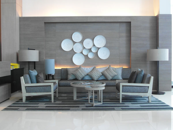 Modern hotel lobby lounge interior with gray sofa, matching armchairs, and a decorative wall feature of white circular plates.