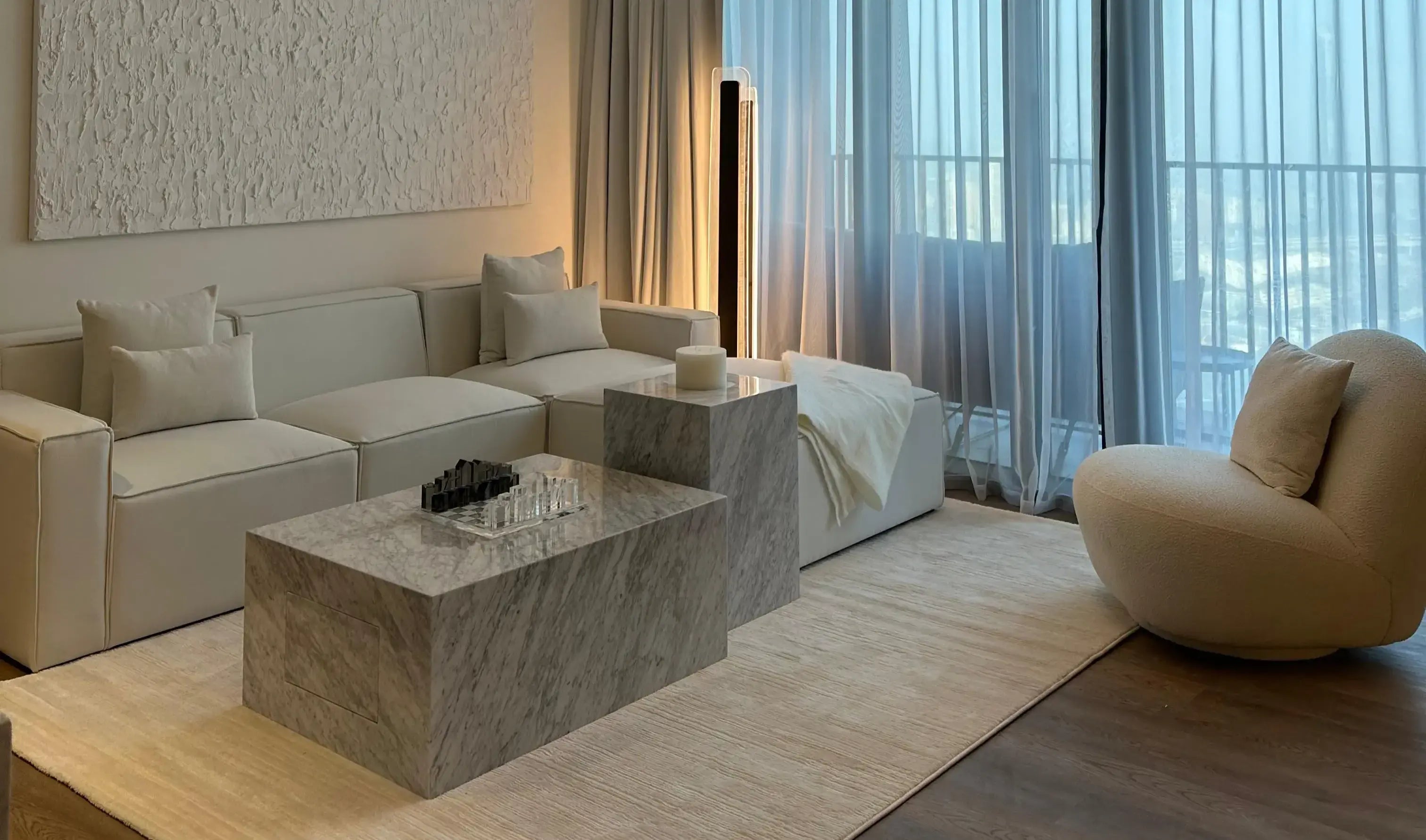 Modern living room with beige sofa, marble coffee table, and large windows.