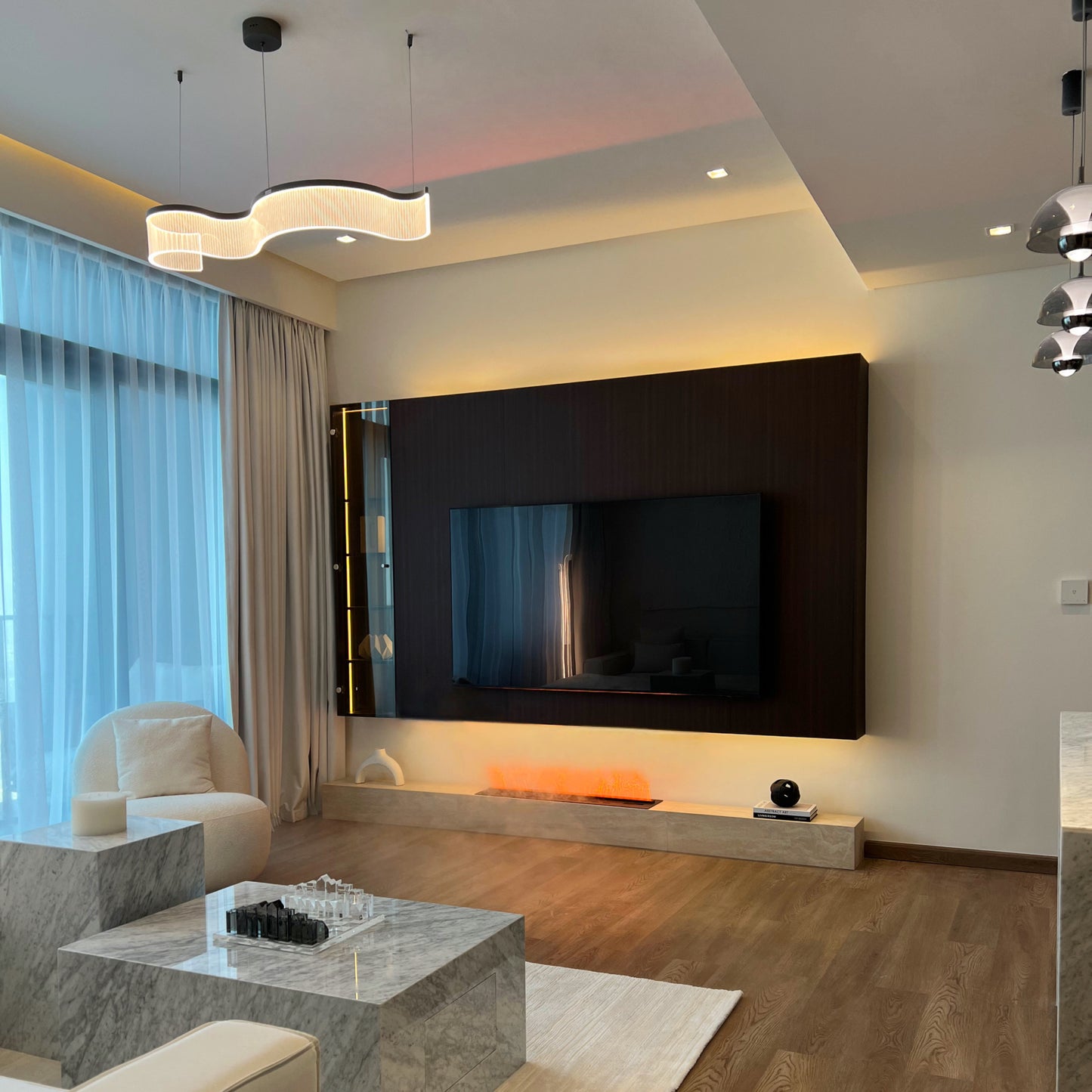 Modern living room with a large TV mounted on the wall, light fixture, and furniture.