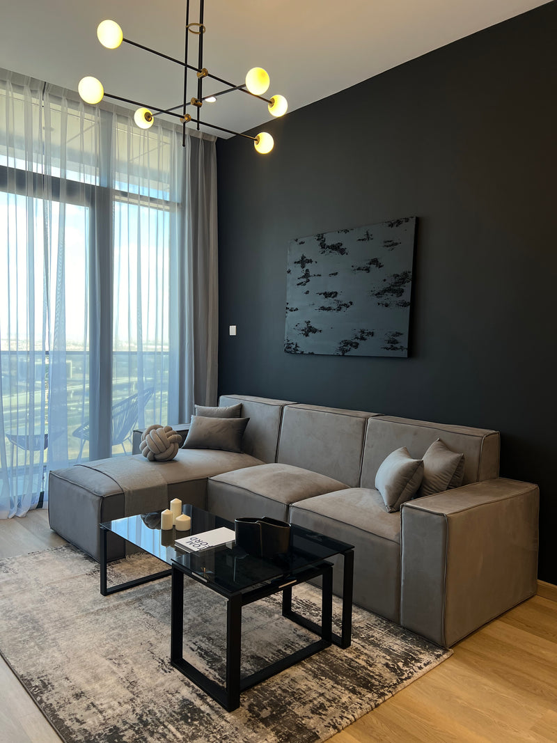Modern living room with gray sectional sofa, black coffee table, and dark wall with abstract art.