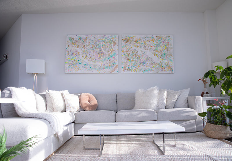 Bright, modern living room with a large gray sectional sofa, white coffee table, and abstract pastel canvas artwork